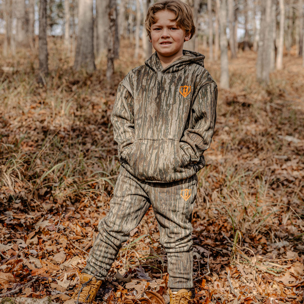 Child wearing a camouflage outfit with a orange BL101 logo in a forest setting