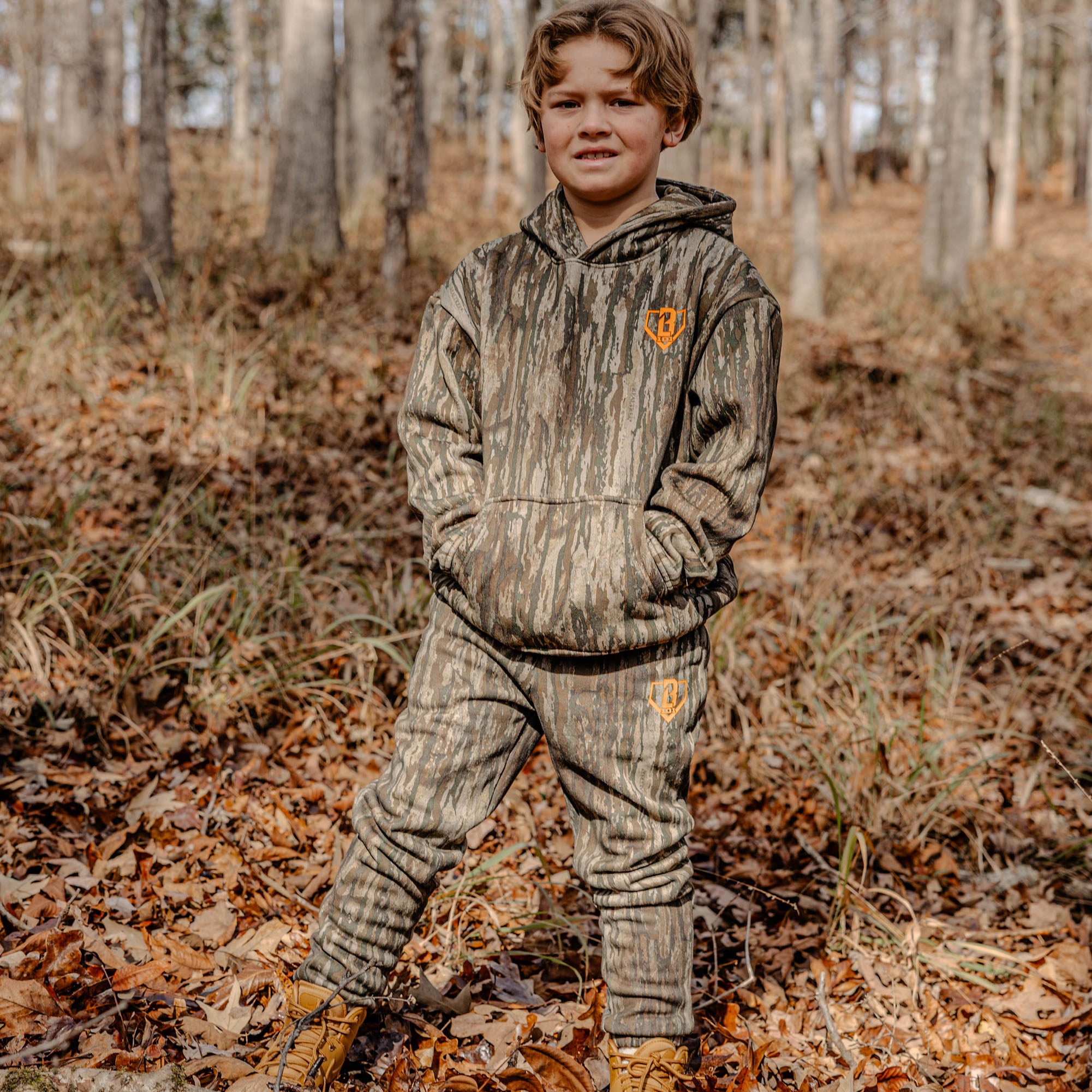 Child wearing a camouflage outfit with a orange BL101 logo in a forest setting