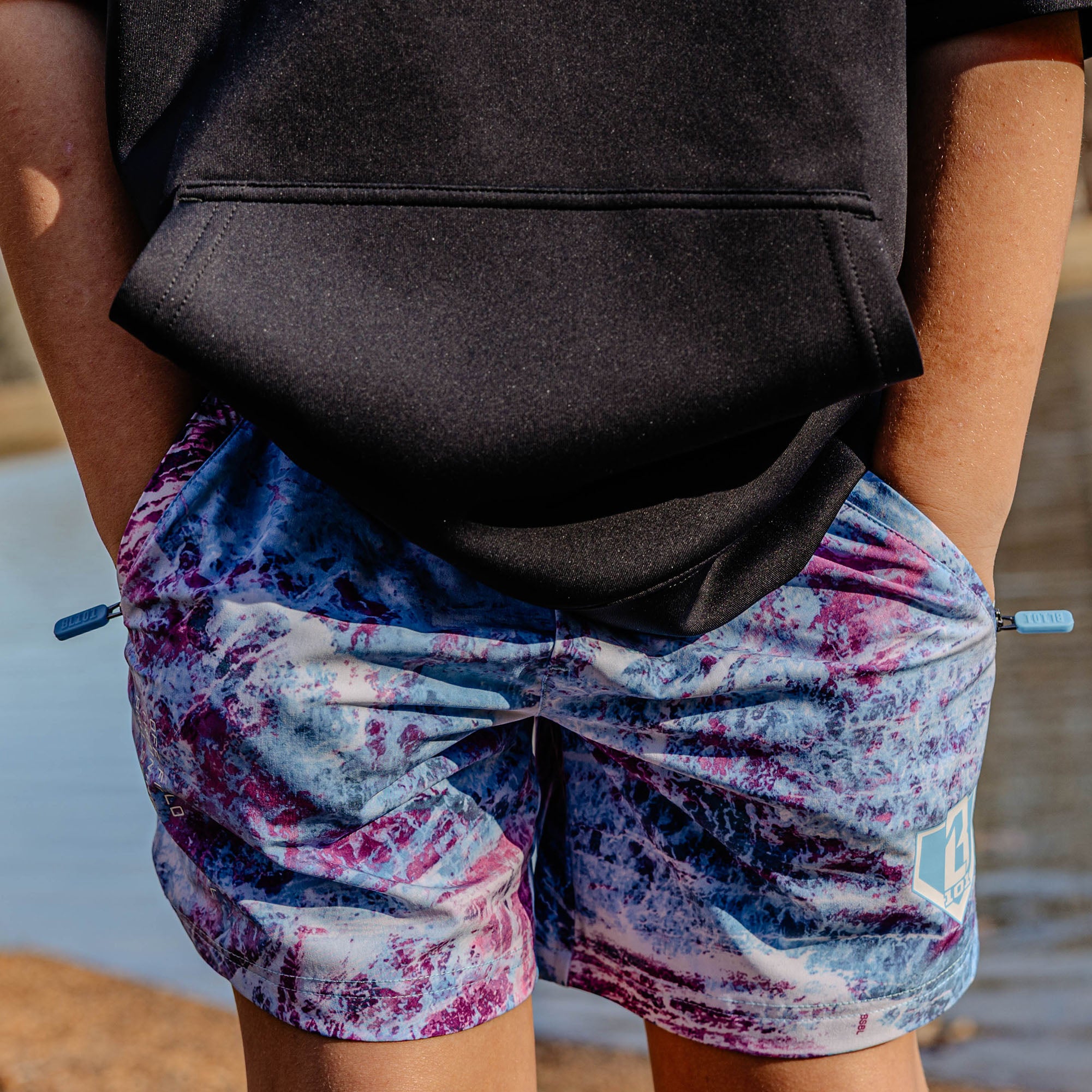 Person wearing a black top with blue and purple shorts .