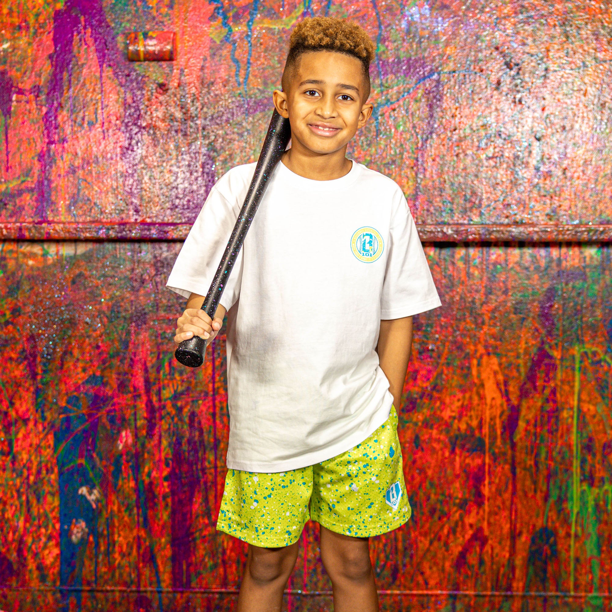 Child holding a baseball bat in front of a colorful, textured wall