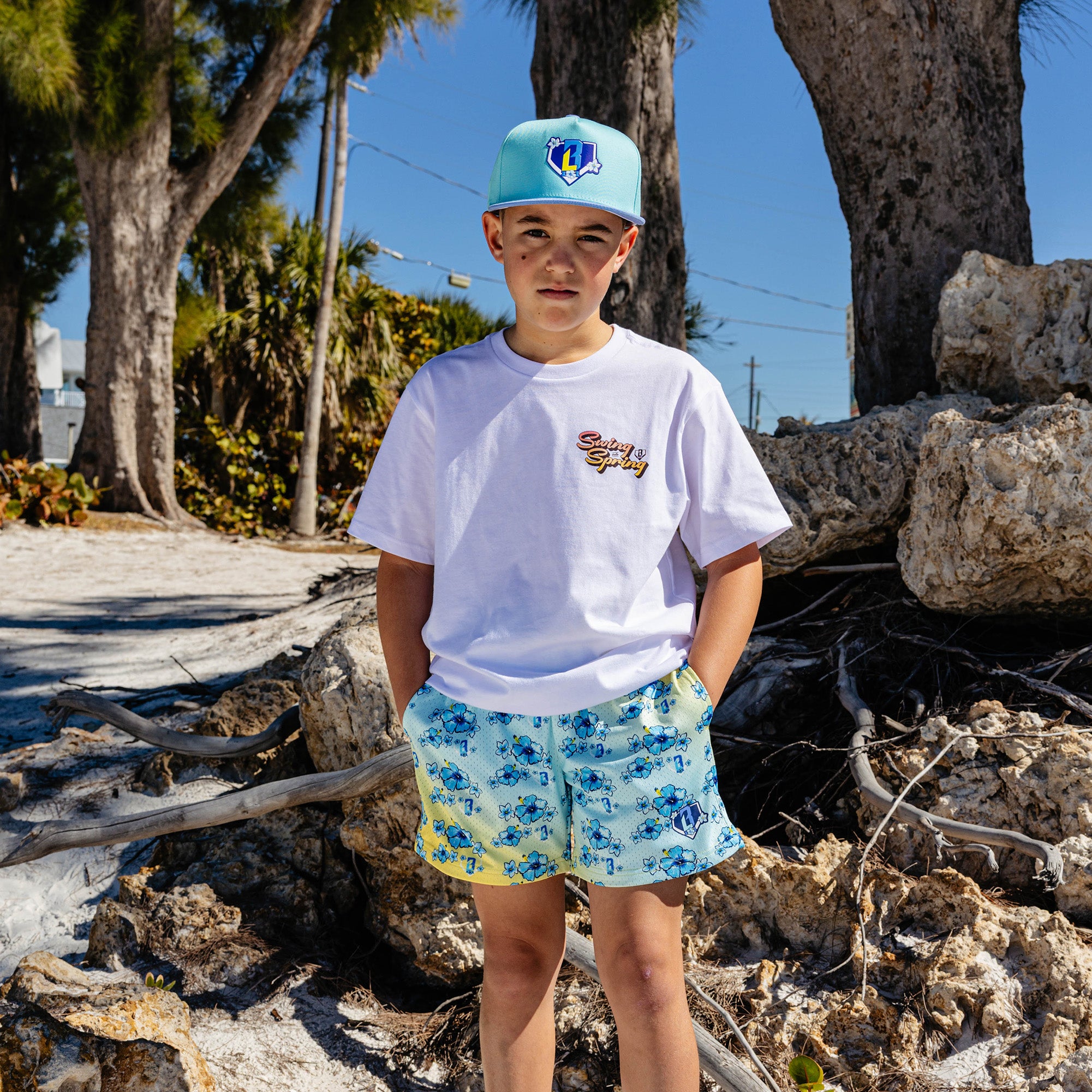Person wearing a white t-shirt with 'Swing into Spring' text and floral shorts standing outdoors with rocks and trees in the background