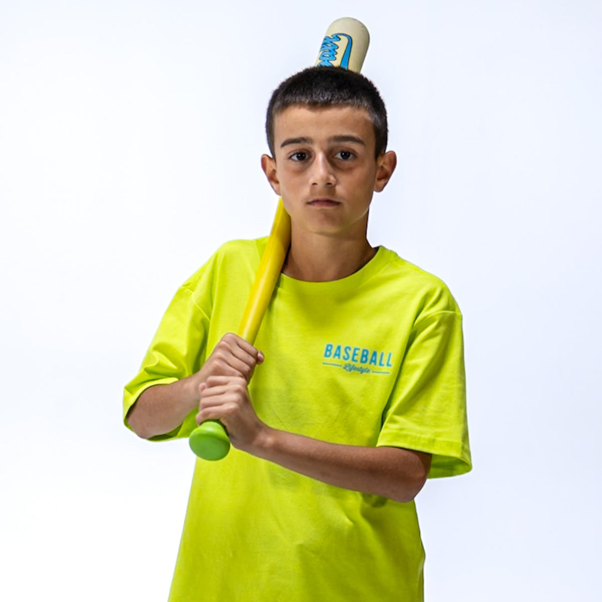 Child wearing a bright yellow 'Baseball Lifestyle' t-shirt holding a bat with a white background