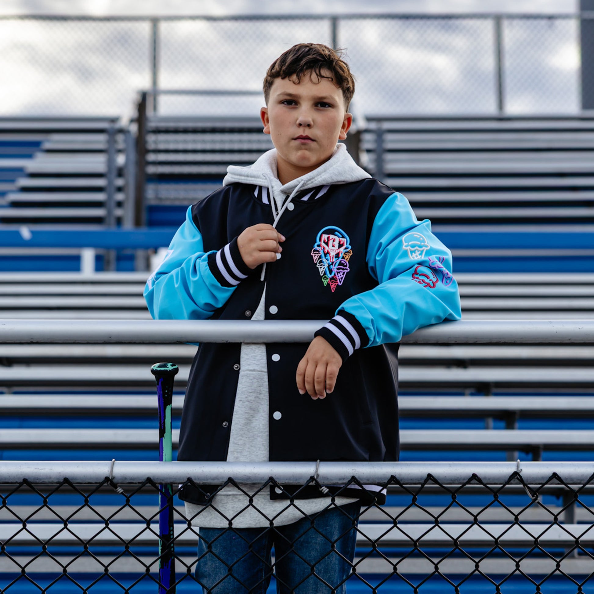 Person wearing a blue and black varsity jacket with a colorful ice cream cones, standing in bleachers.