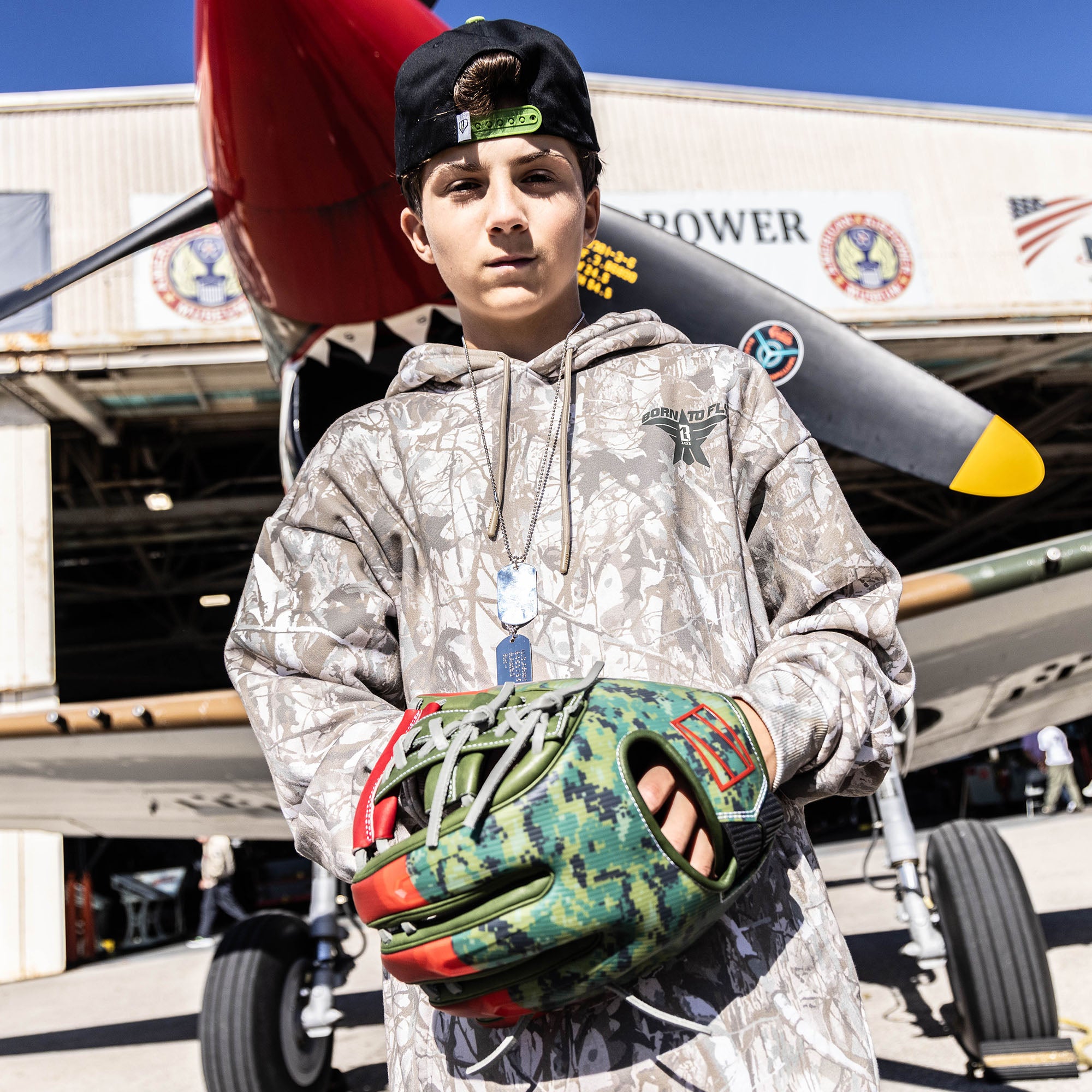 Person holding a camouflage baseball glove in front of an airplane