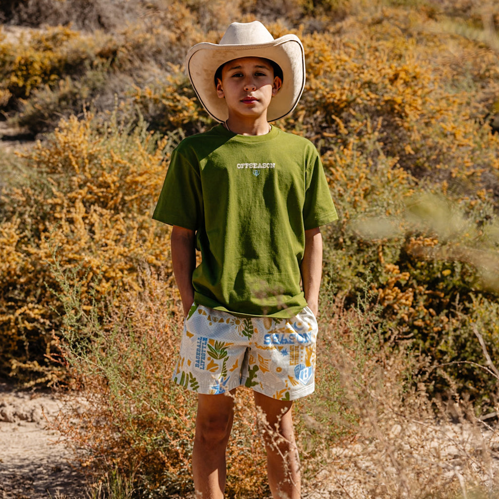 Person wearing a green 'OFFSEASON' t-shirt and desert patterned shorts standing in a desert-like environment.