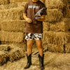 Person wearing a brown shirt and cow print shorts standing in front of hay bales.
