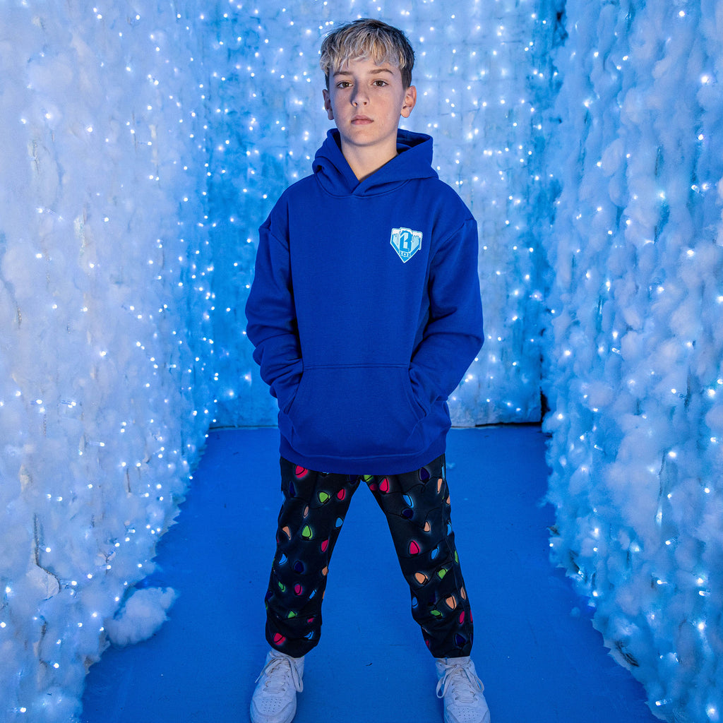 Person wearing a blue BL101 hoodie with black jogger pants with colorful Christmas lights in a blue-themed indoor setting
