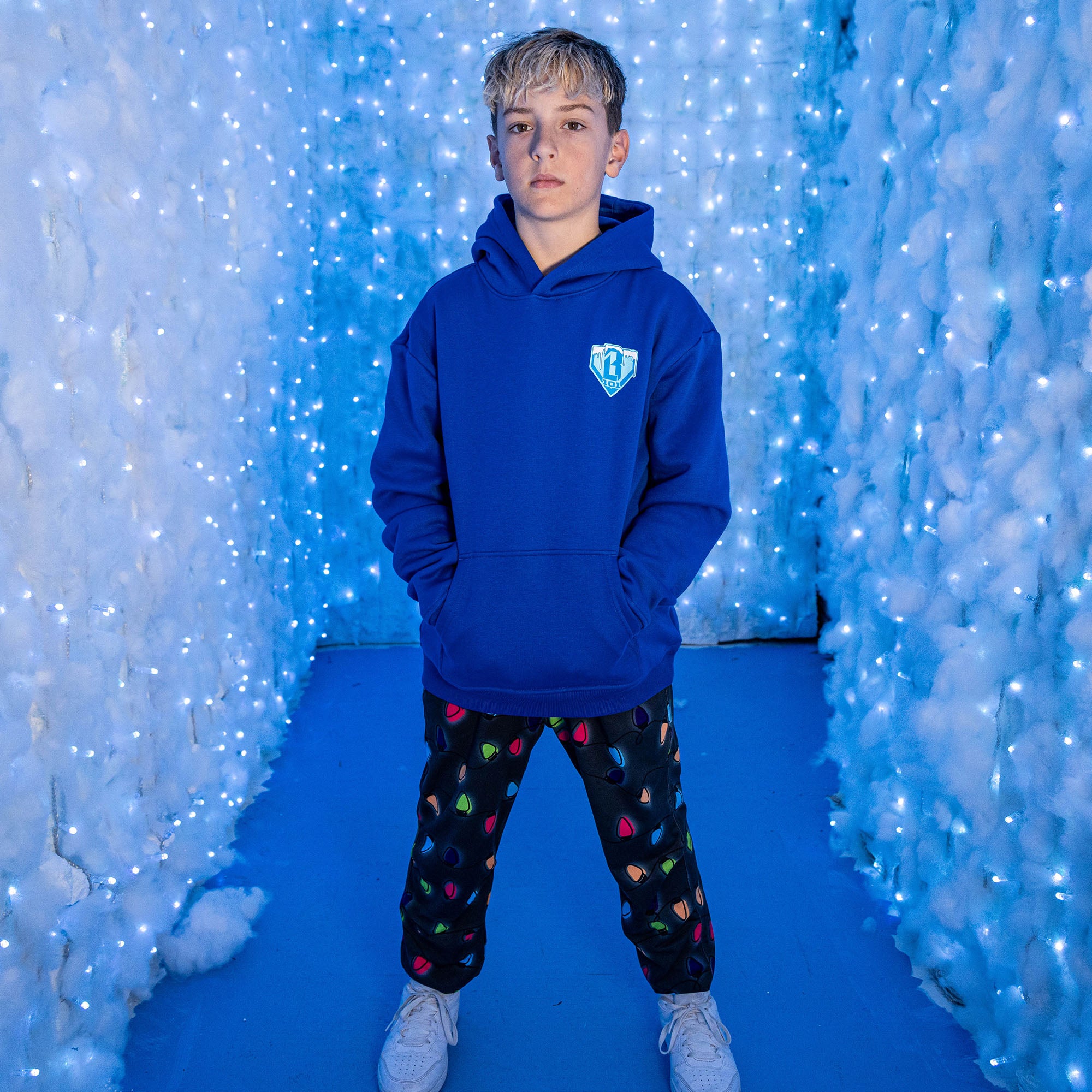 Person wearing a blue BL101 hoodie with black jogger pants with colorful Christmas lights in a blue-themed indoor setting