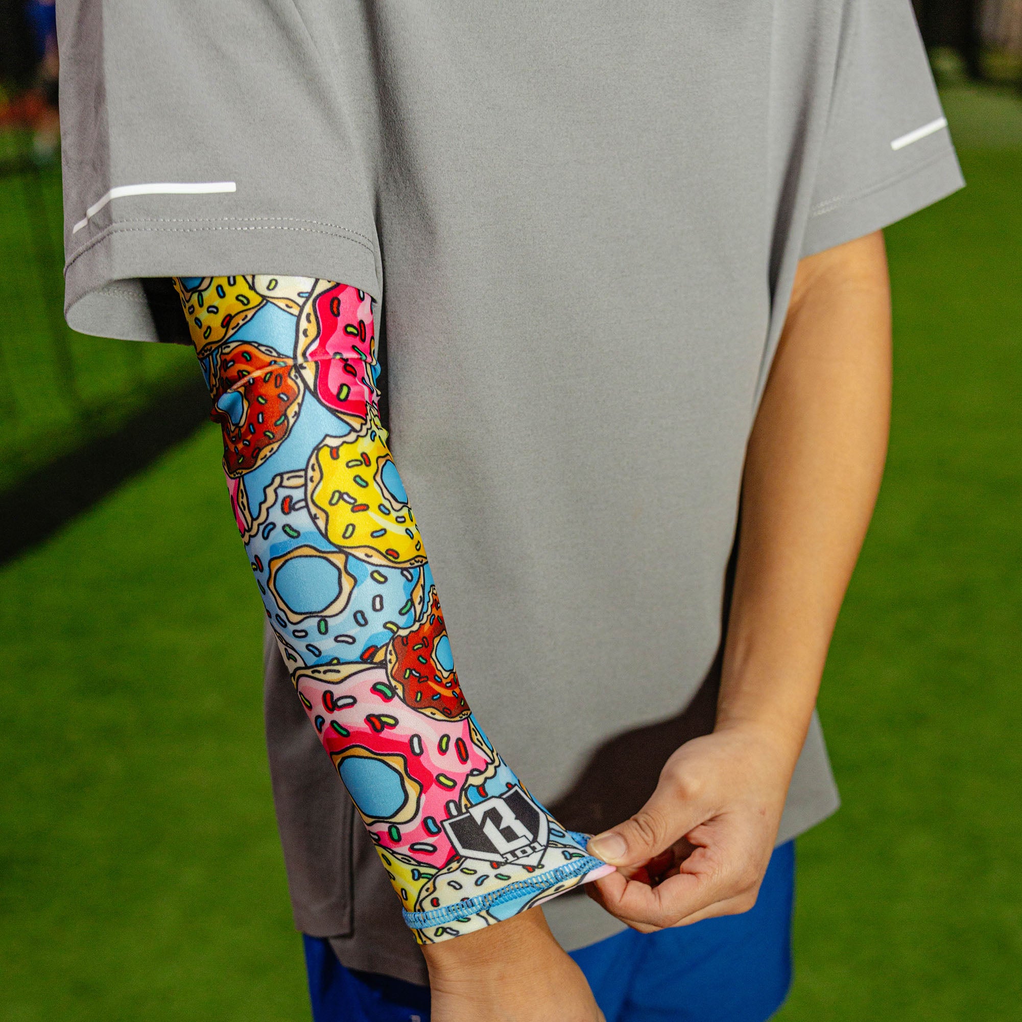 Close-up of a youth player wearing the donut arm sleeve on their right arm being pulled down at the wrist against a gray shirt