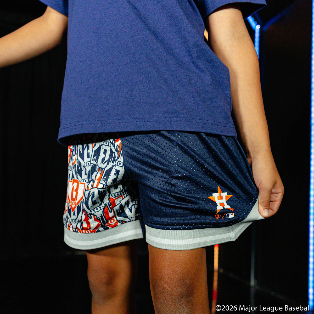 Youth model wearing blue youth shorts with "Houston Astros Sticker Court" design