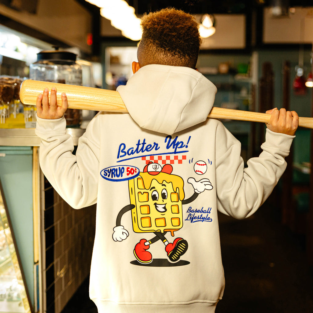 Person wearing a hoodie with a cartoon waffle character and 'Batter Up!' text, holding a baseball bat.