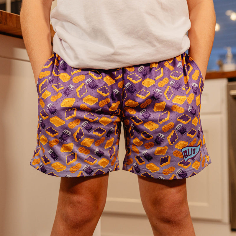 Close-up front view of BL101 youth purple PB&J print mesh shorts showing the all-over sandwich and peanut graphic with BL101 logo.