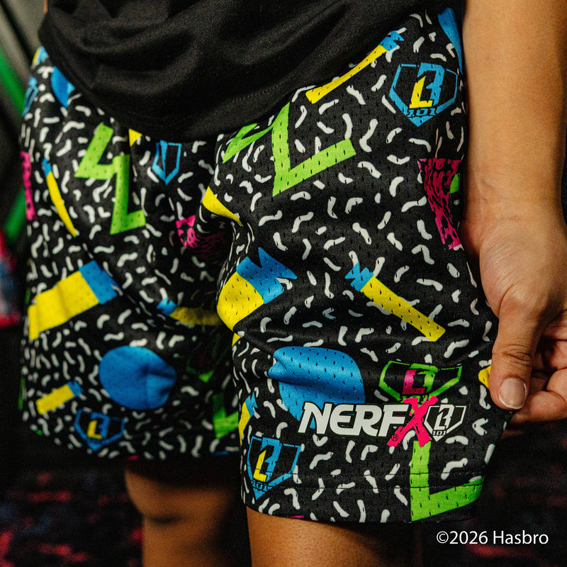 Child wearing a black 'NERF X BL101' t-shirt and colorful shorts standing in front of green and black background