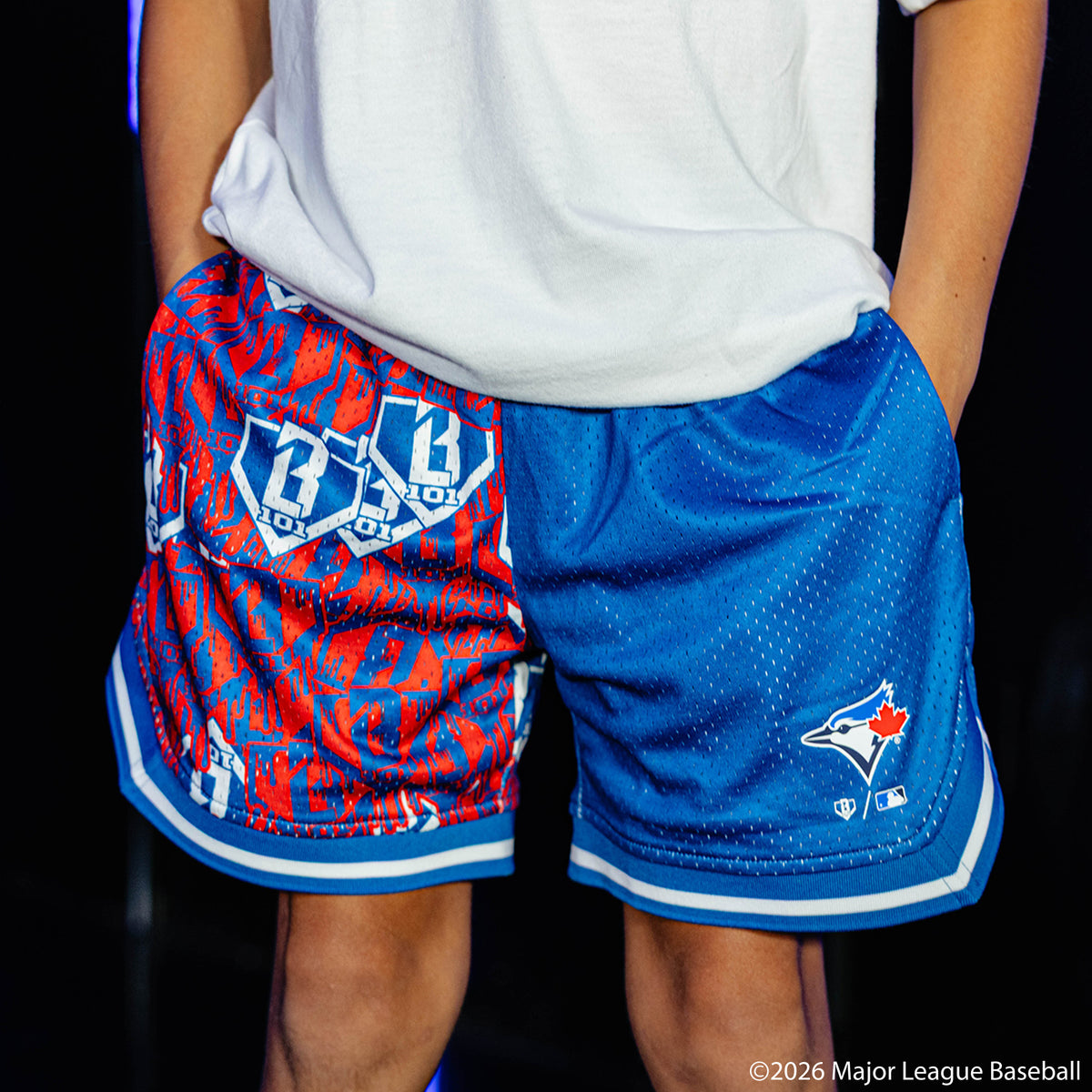 Youth model wearing blue youth shorts with "Toronto Blue Jays Sticker Court" design