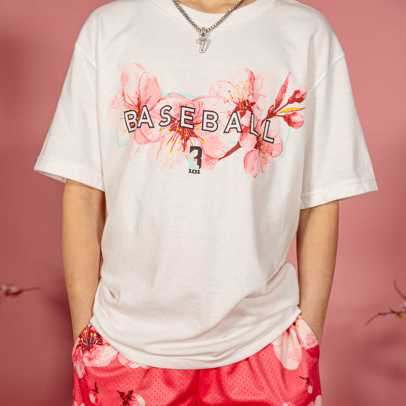 Close up of the cherry blossom Baseball graphic on a white BL101 tee worn by a young boy with pink floral shorts against a pink background