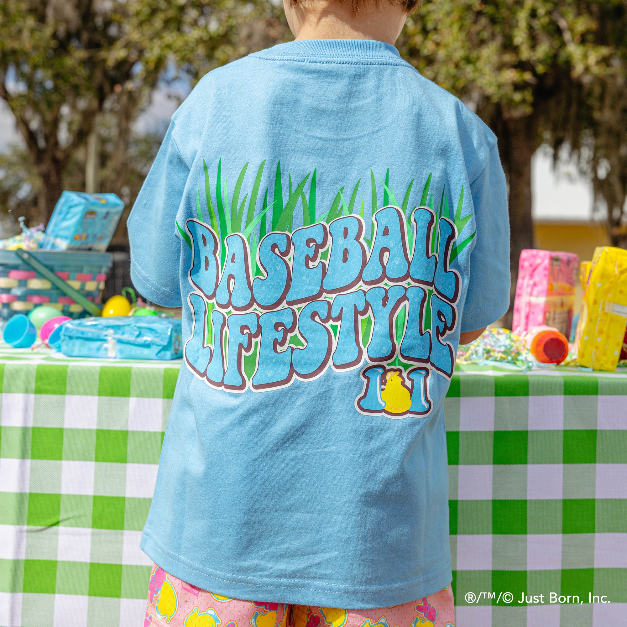 Person wearing a blue t-shirt with 'Baseball Lifestyle' peeps text at an outdoor event.