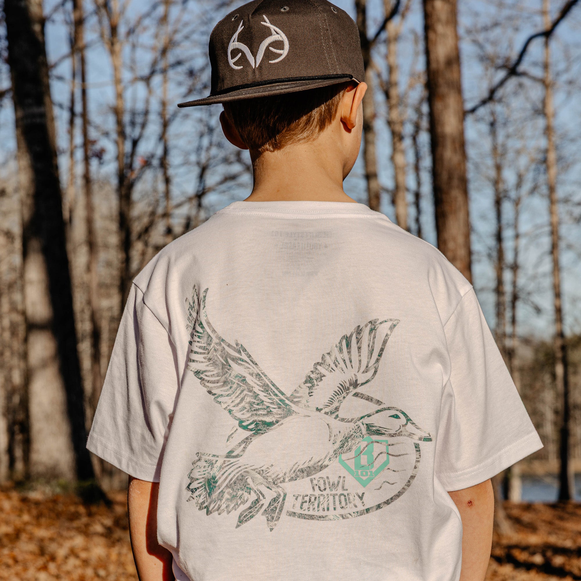 Youth model wearing white youth graphic tee with “Fowl Territory” design