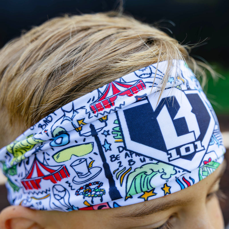 Close-up of the Jackson Olson x BL101 white headband showing the all-over comic-style graphic print and BL101 shield logo