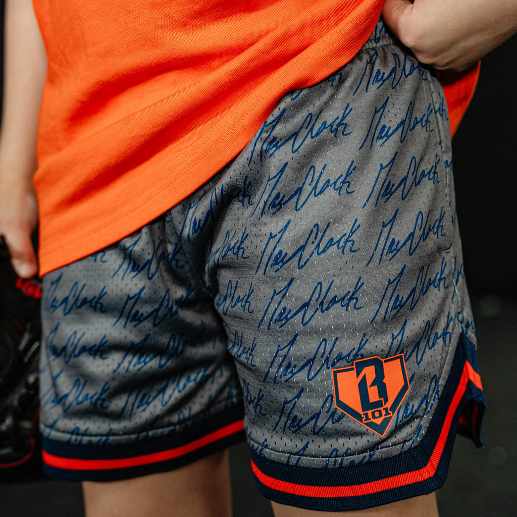 Person wearing gray shorts with blue text and orange accents, standing against a dark background.