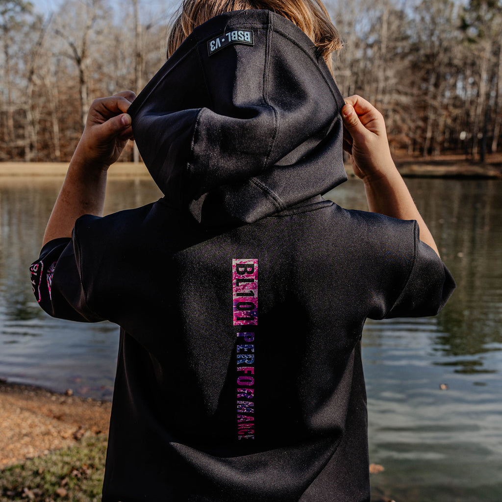 Person wearing a black hoodie with'BL101 PERFORMANCE' logo, standing by a lake.