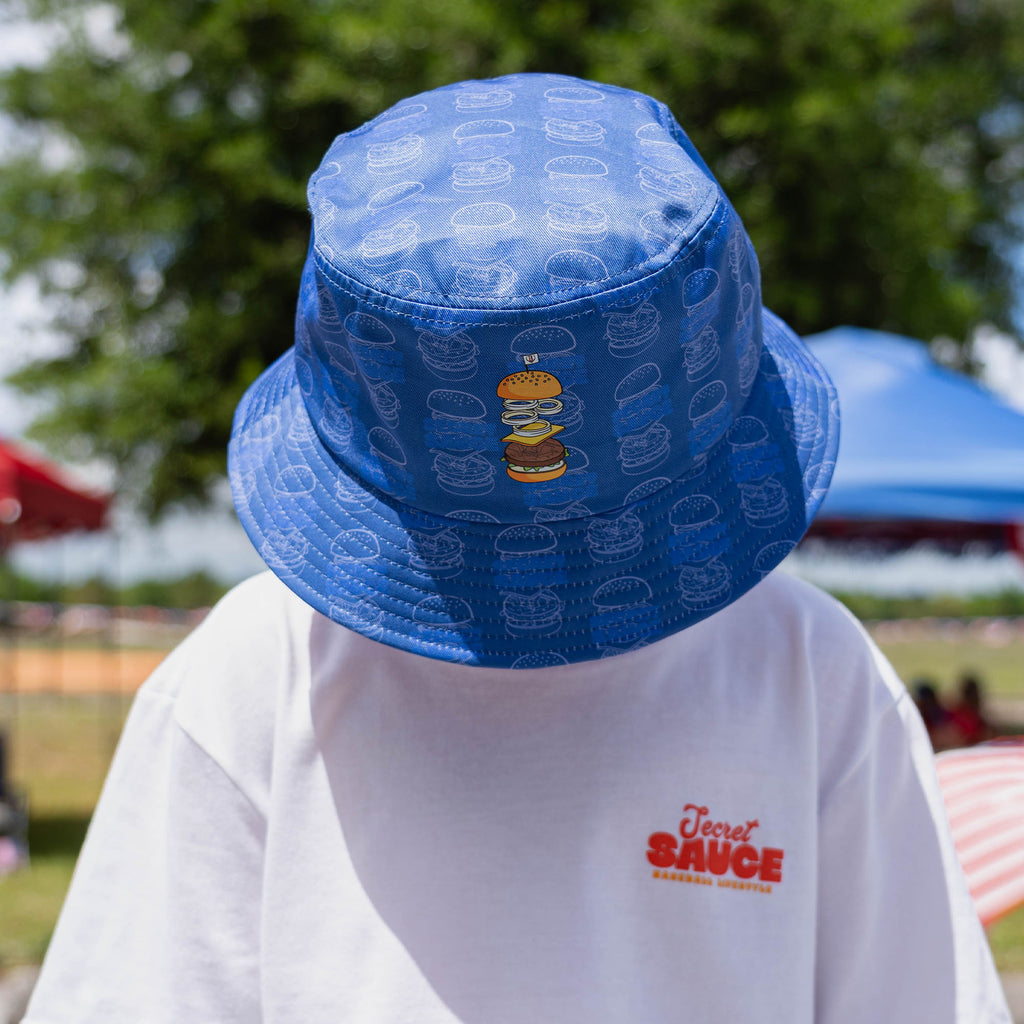 Person wearing a blue bucket hat with a burger pattern and a white shirt with 'Secret Sauce' text.