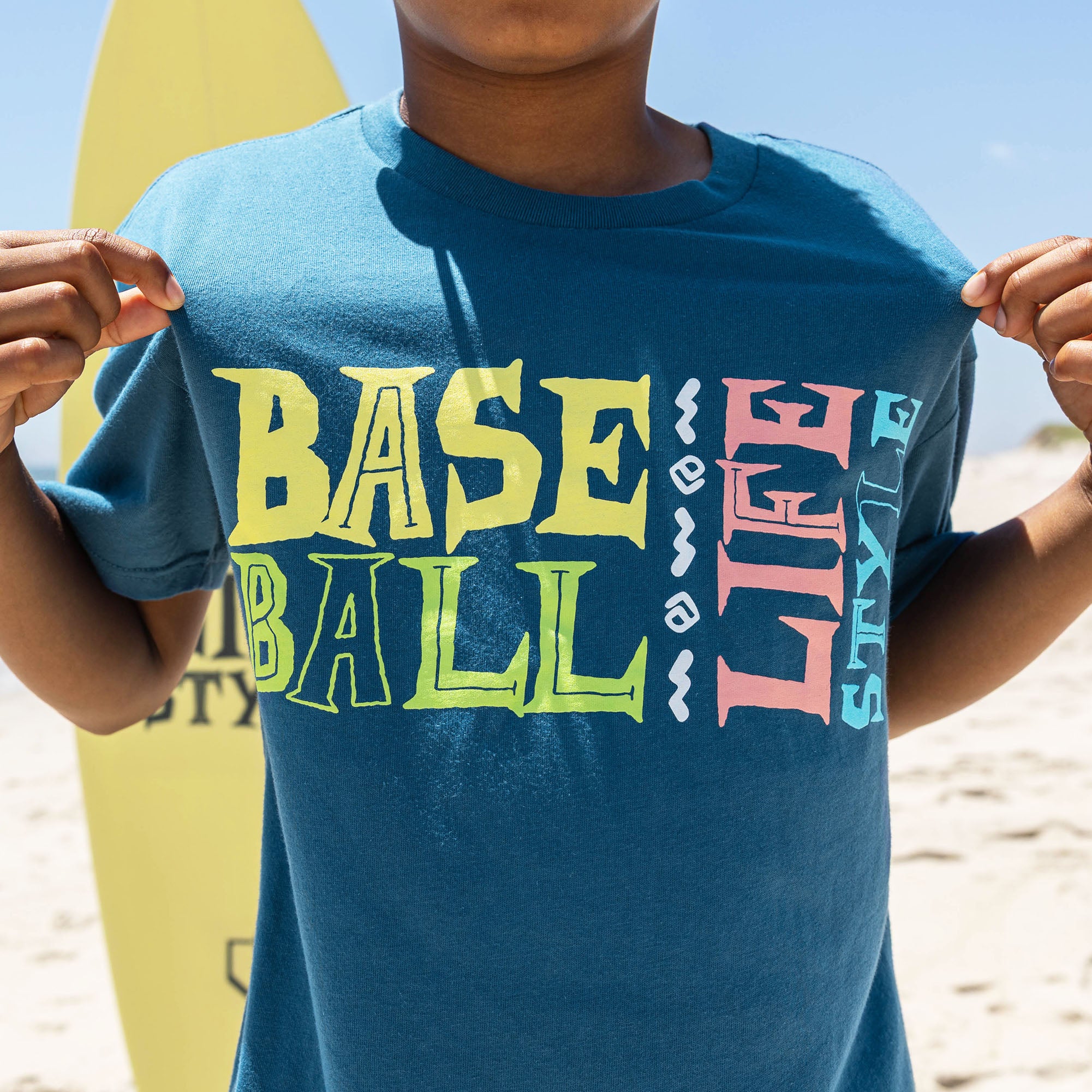 Youth model wearing blue youth graphic tee with "Surfside Slugger" design