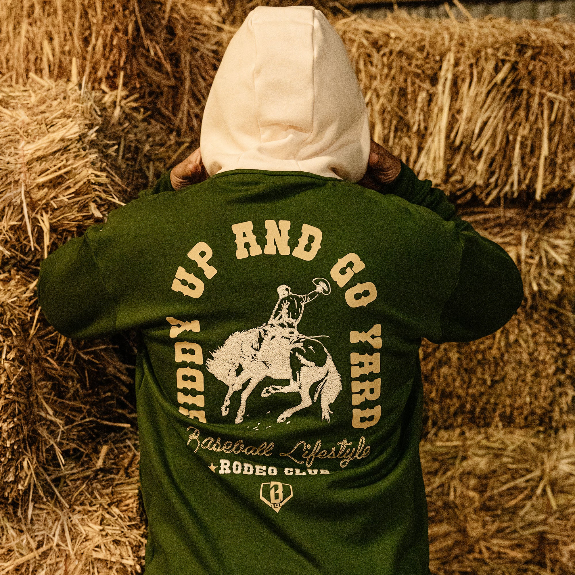 Person wearing a green hoodie with 'Giddy Up and Go' text and graphics, standing among hay bales.
