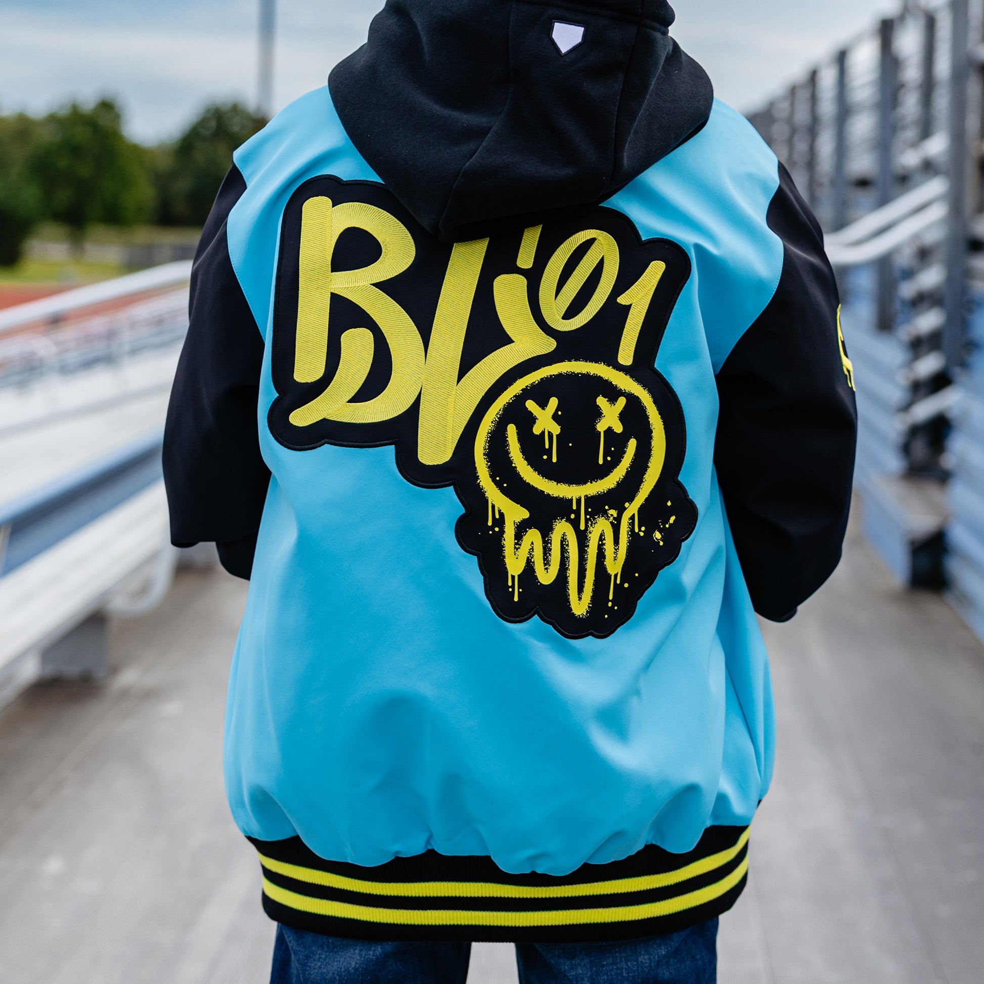 Person wearing a blue and black jacket with yellow BL101 logo outdoors