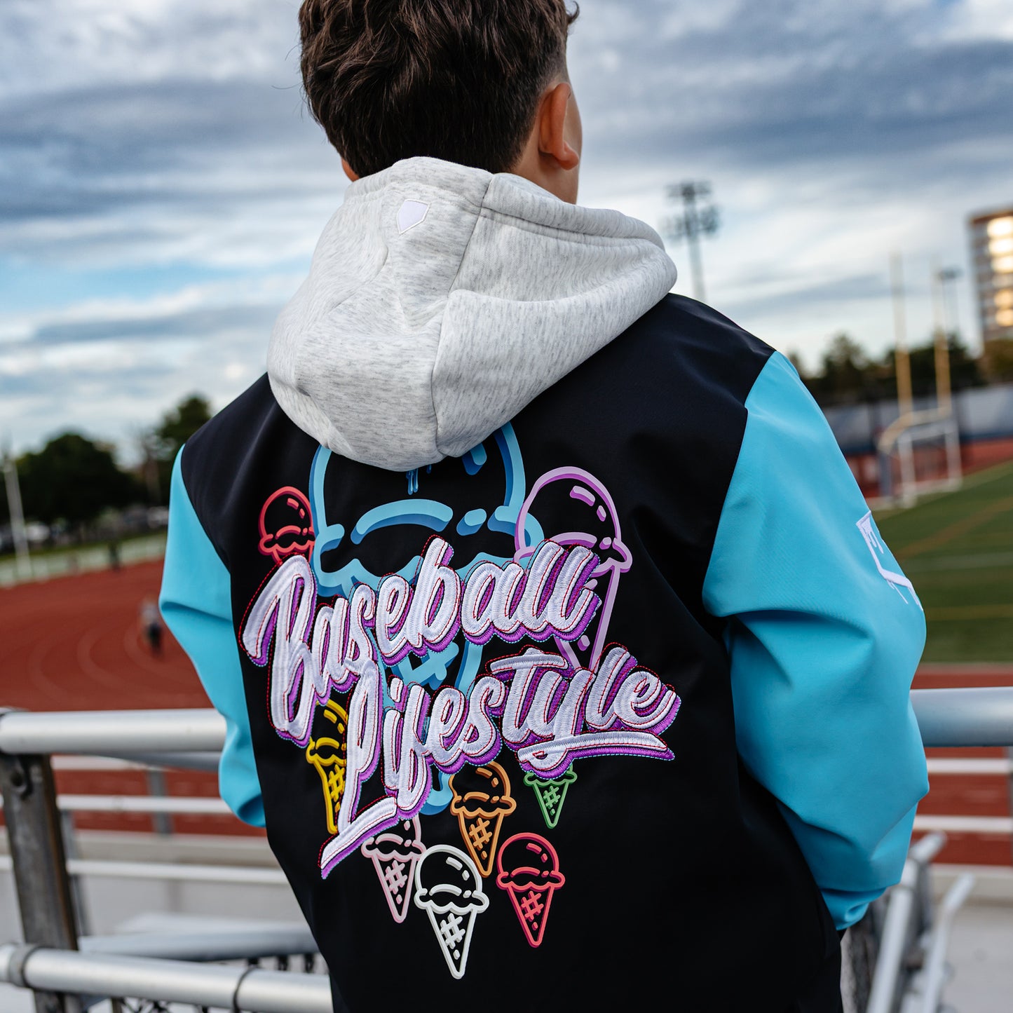 Person wearing a black and blue jacket with 'Baseball Lifestyle' logo and colorful cones outdoors.