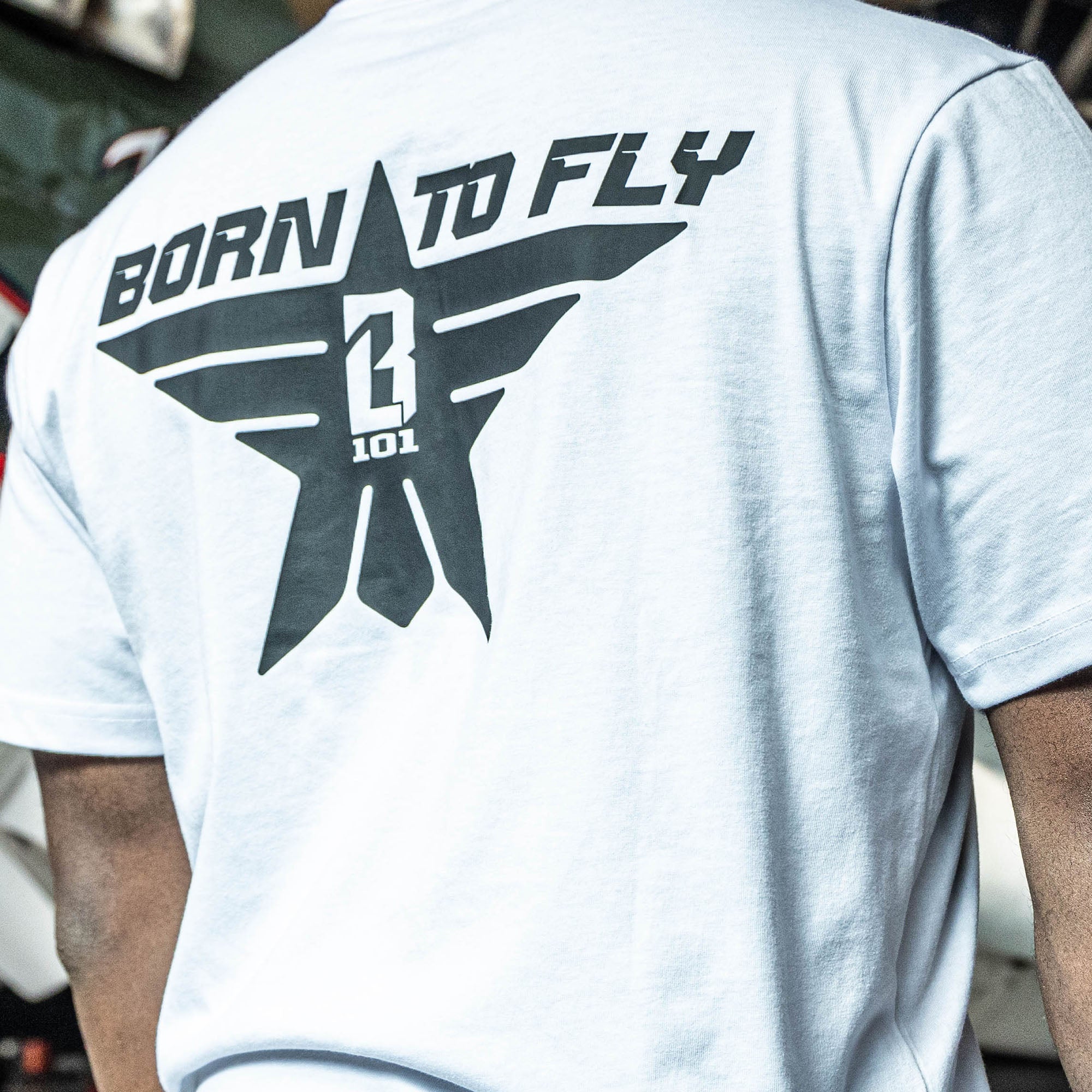 Close up of Youth white t-shirt with black “BORN TO FLY” lettering, black star, and white BL101 logo centered inside the star on person