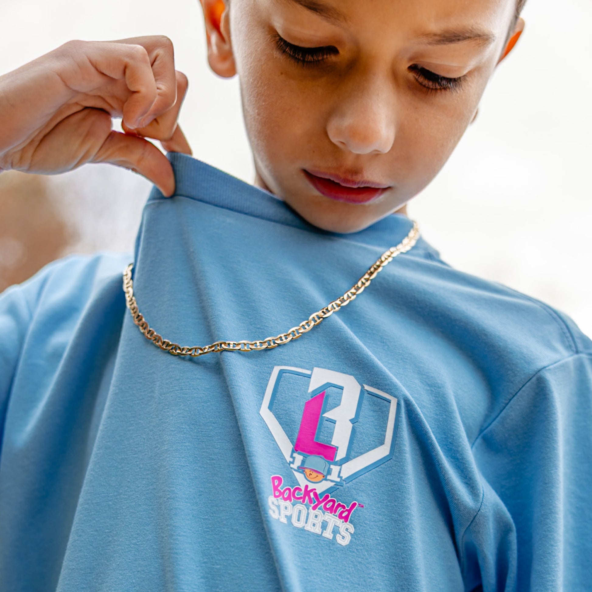 Child wearing a blue shirt with a BL101 logo and Backyard Sports text, holding a gold chain.