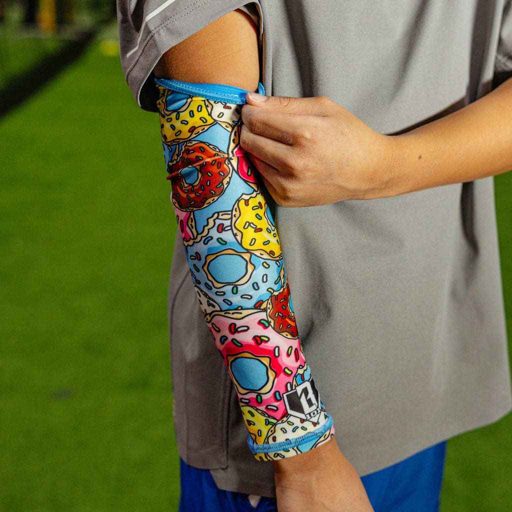 Close-up of the donut arm sleeve being pulled up at the bicep showing the blue elastic band at the top against a gray shirt outdoors