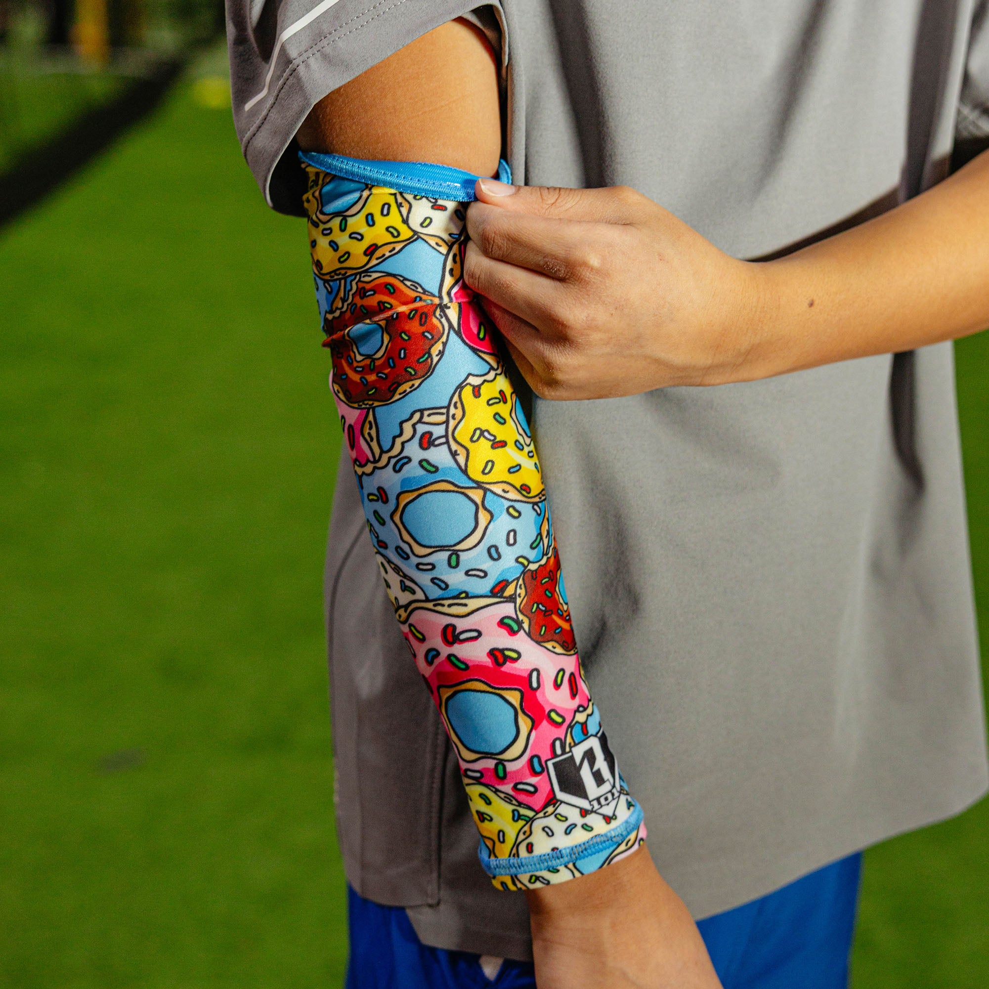 Close-up of the donut arm sleeve being pulled up at the bicep showing the blue elastic band at the top against a gray shirt outdoors