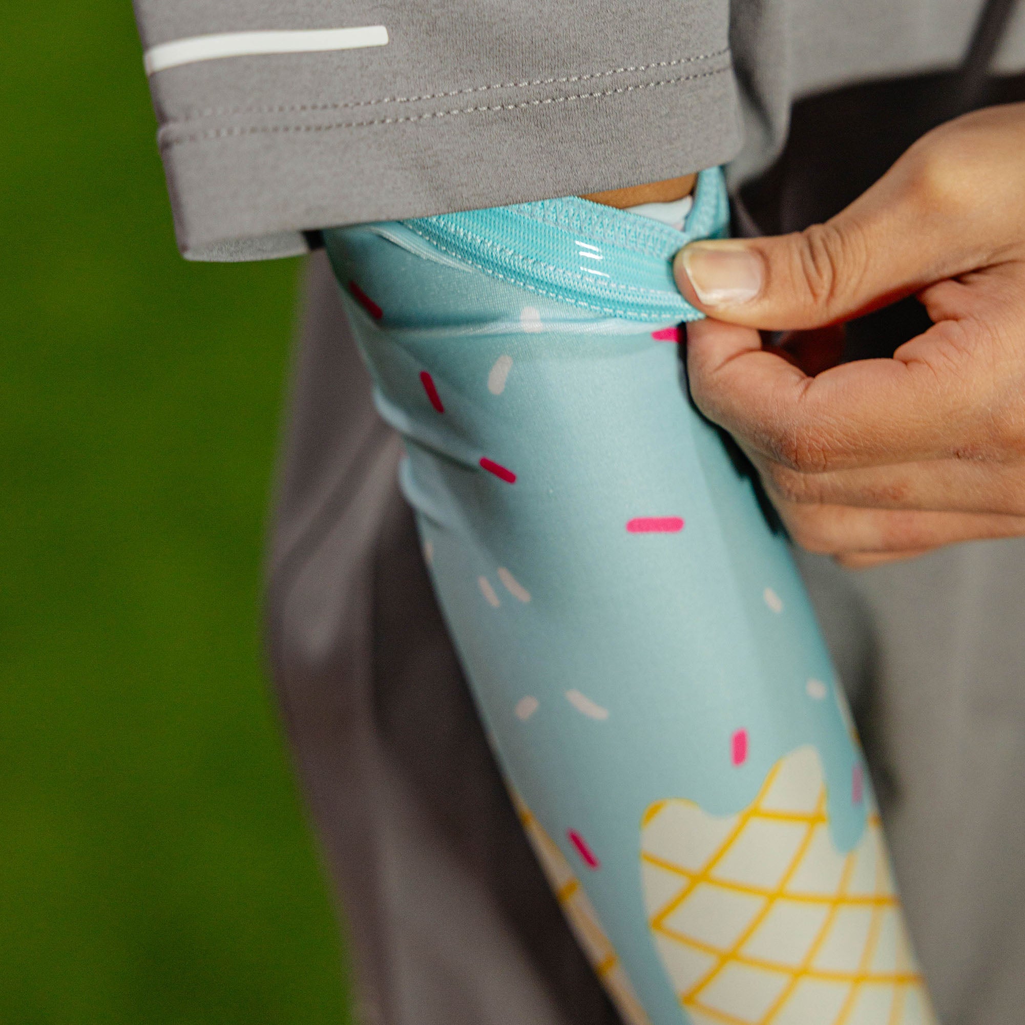 Close-up of the cotton candy ice cream arm sleeve being pulled up at the bicep showing the light blue elastic band and sprinkle print against a gray shirt outdoors