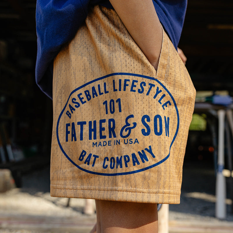 Side detail shot of the brown youth BL101 Bat Co Shorts highlighting the large Father & Son Bat Company oval stamp graphic on the left leg.