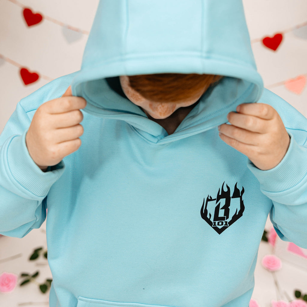 Child wearing a light blue hoodie with a black BL101 logo against a decorative background with hearts.