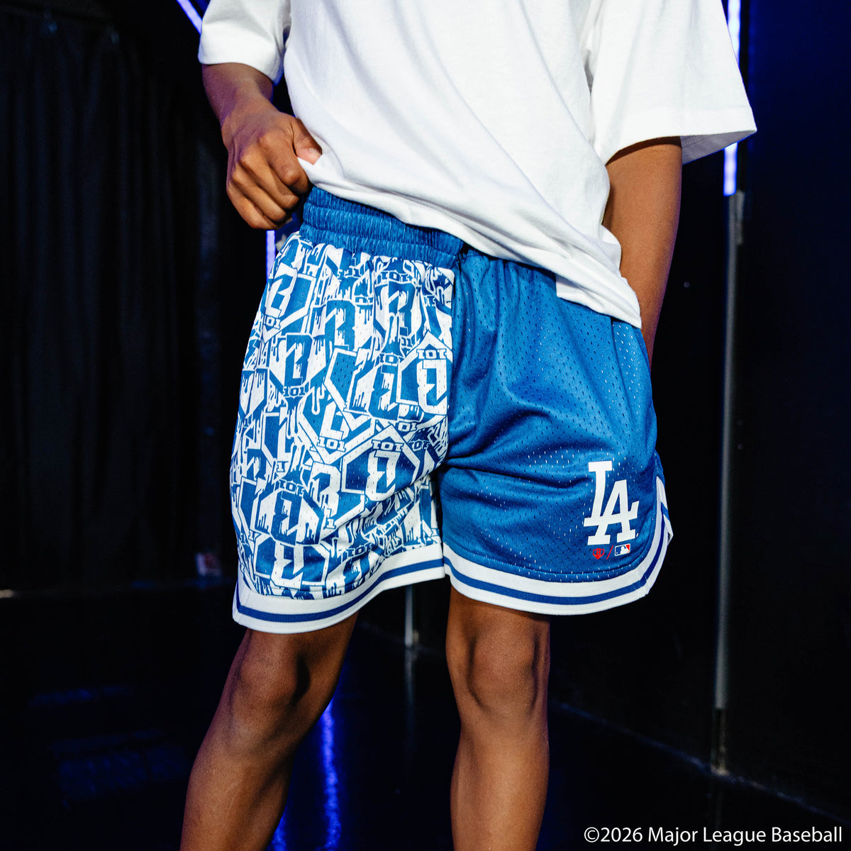 Youth model wearing blue youth shorts with "Los Angeles Dodgers Sticker Court" design