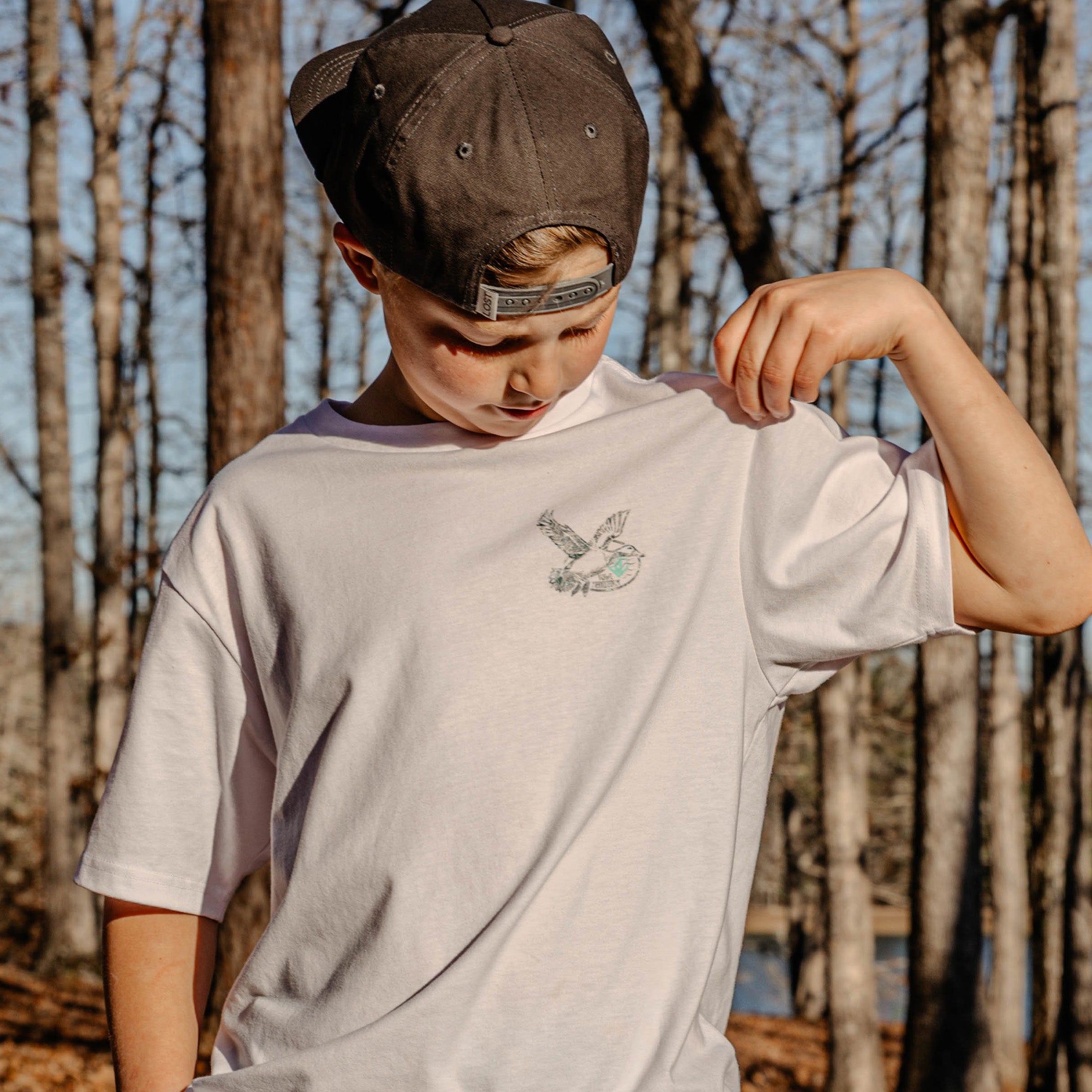 Youth model wearing white youth graphic tee with “Fowl Territory” design