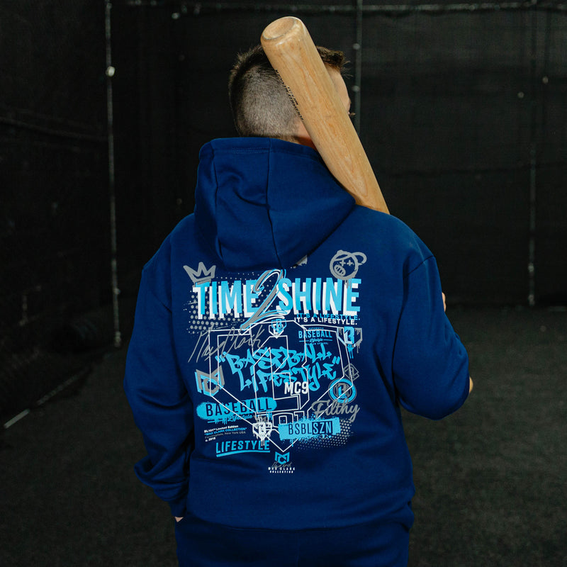 Person wearing a blue hoodie with text and graphics, holding a baseball bat against a dark background.