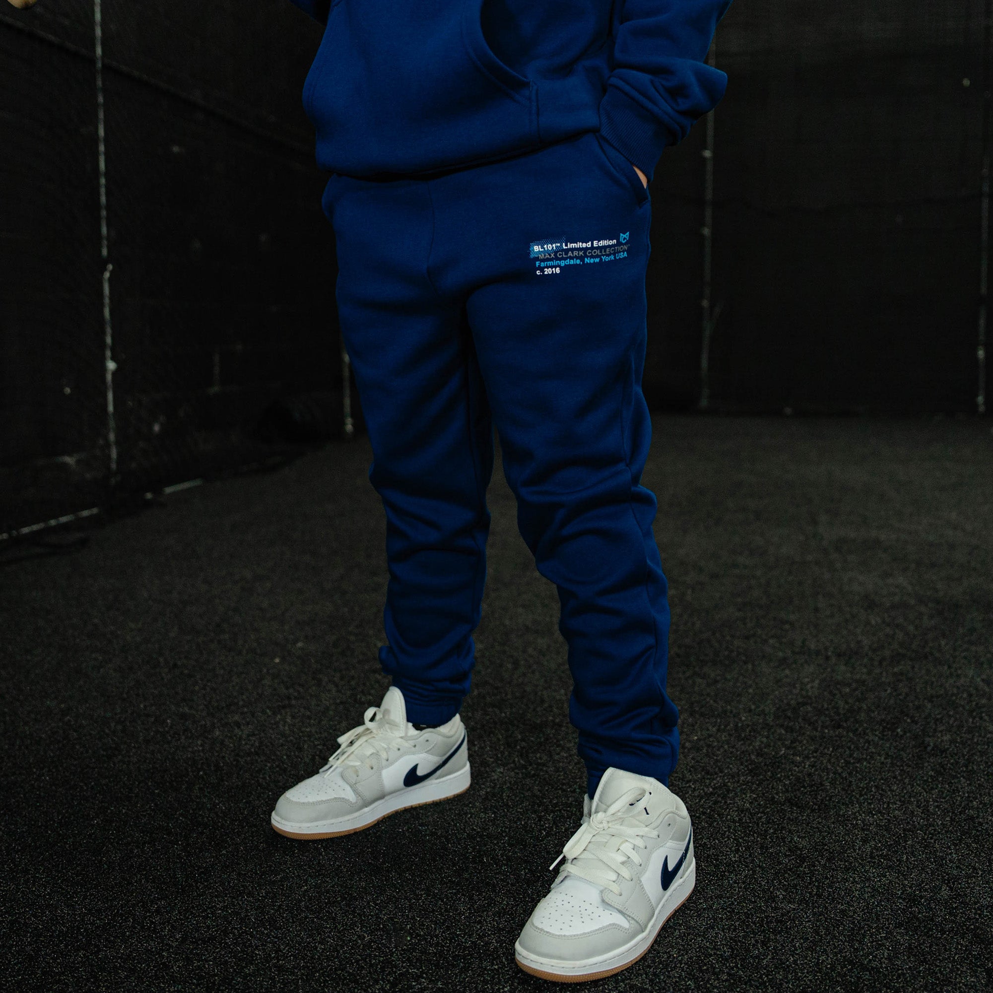 Person wearing a blue tracksuit with white sneakers on a dark background
