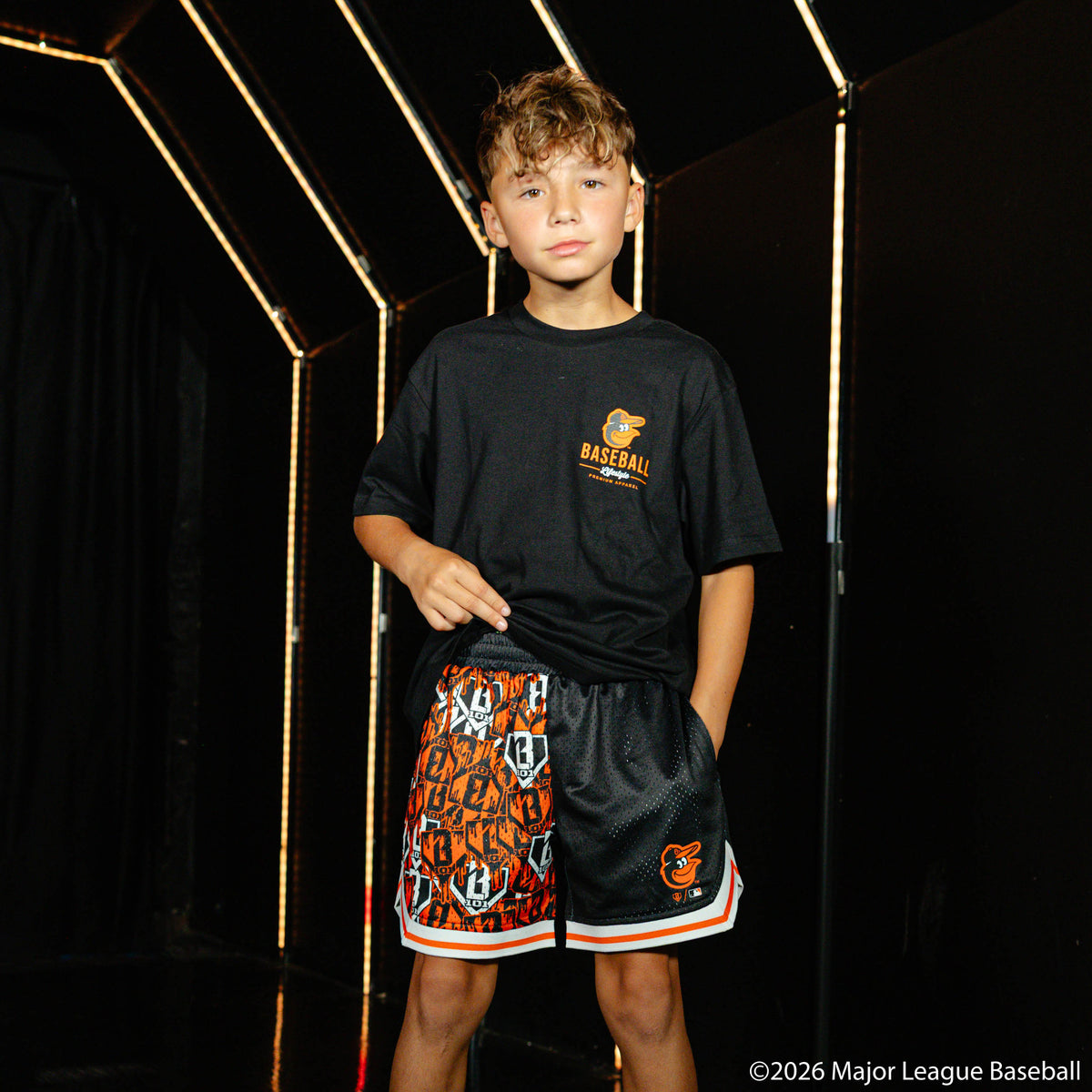 Youth model wearing black youth shorts with "Baltimore Orioles Sticker Court" design