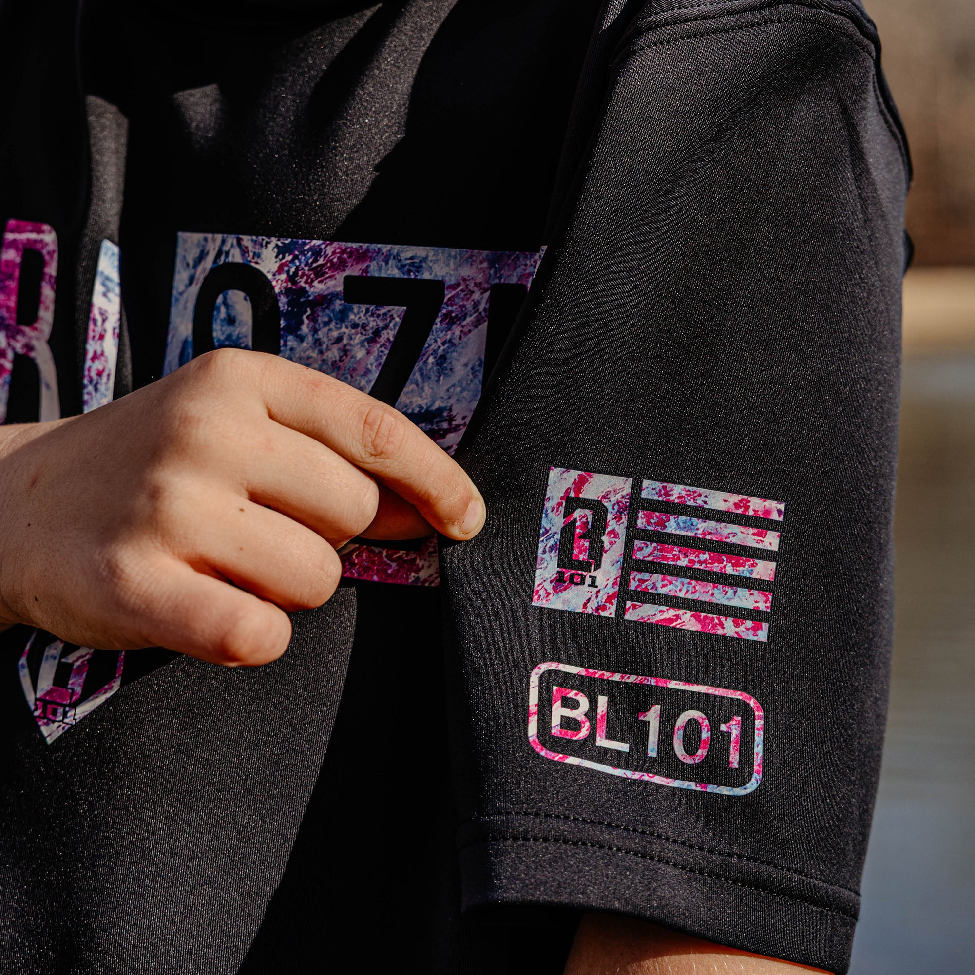 Black hoodie with colorful 'BL101' logo on sleeve, held by a person.