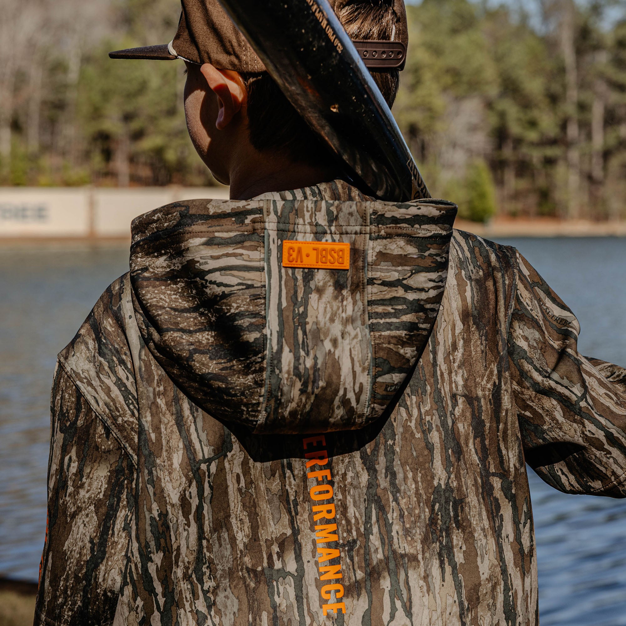 Person wearing a camouflage jacket with orange 'BSBL V3' text in an outdoor setting