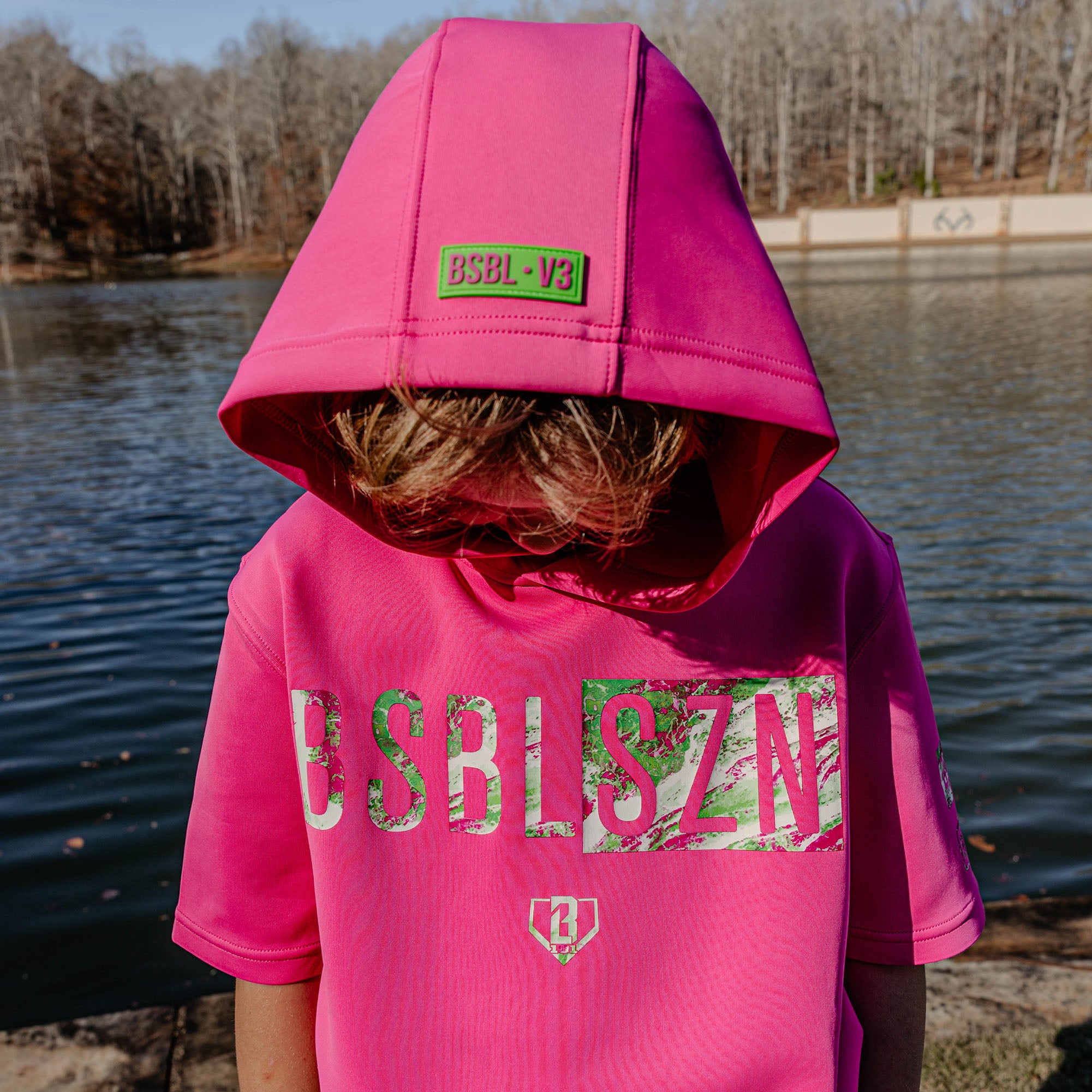 Person wearing a pink hoodie with 'BSBL V3' branding by a body of water.