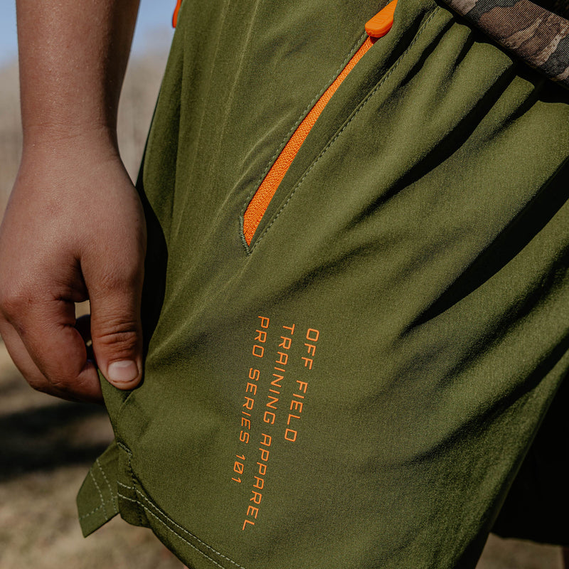 Green shorts with orange zippers and text on a blurred natural background