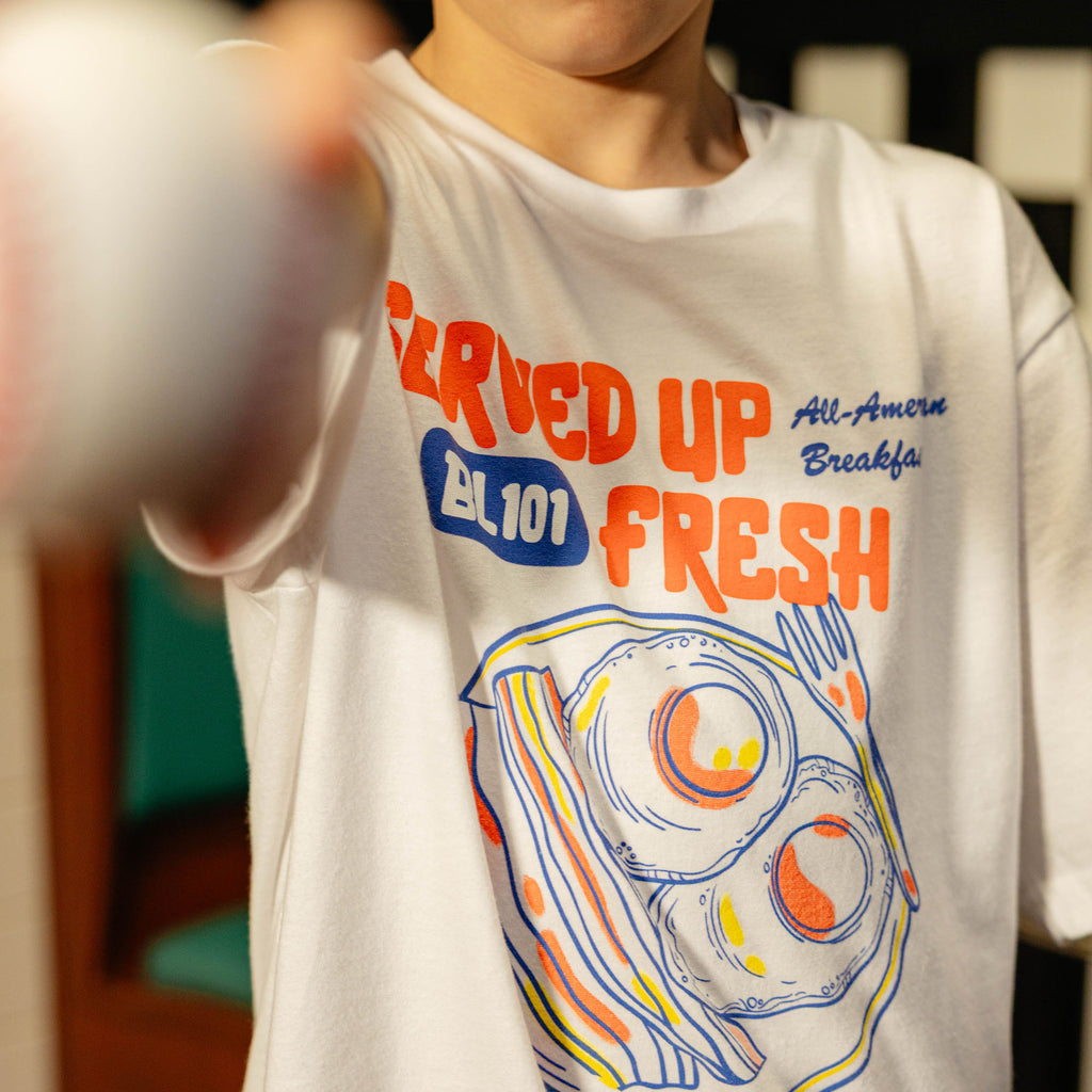 Close up of white t-shirt with a bacon and egg graphic and 'Served Up BL101 Fresh' text