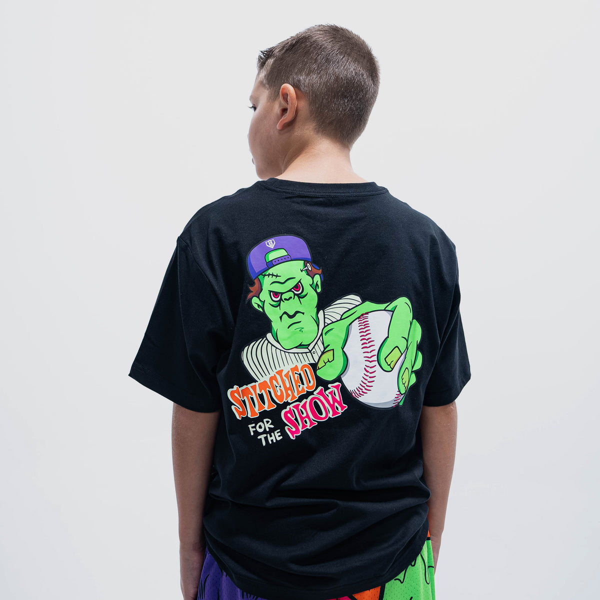 Youth model wearing black youth graphic tee with "Stitched For The Show" design