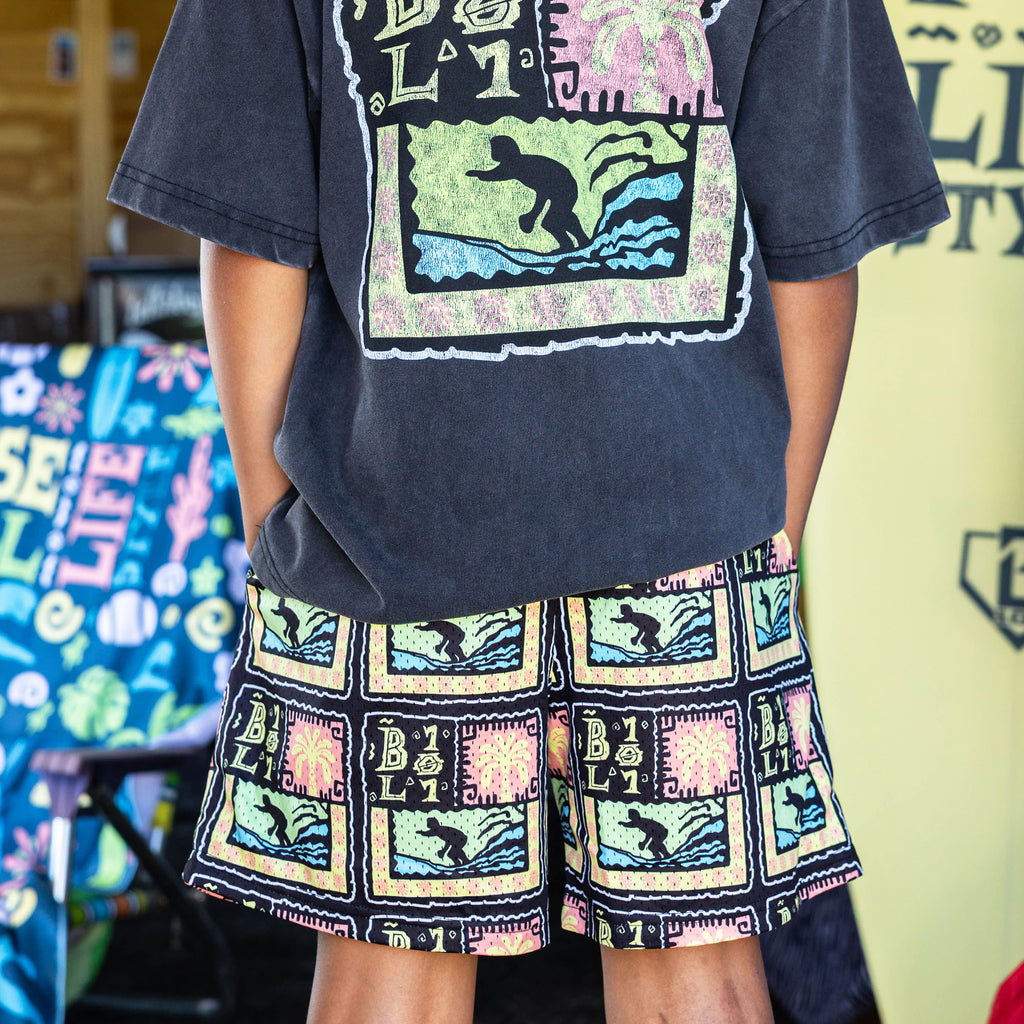 Youth model wearing multi-color youth shorts with "Wave Goodbye" design