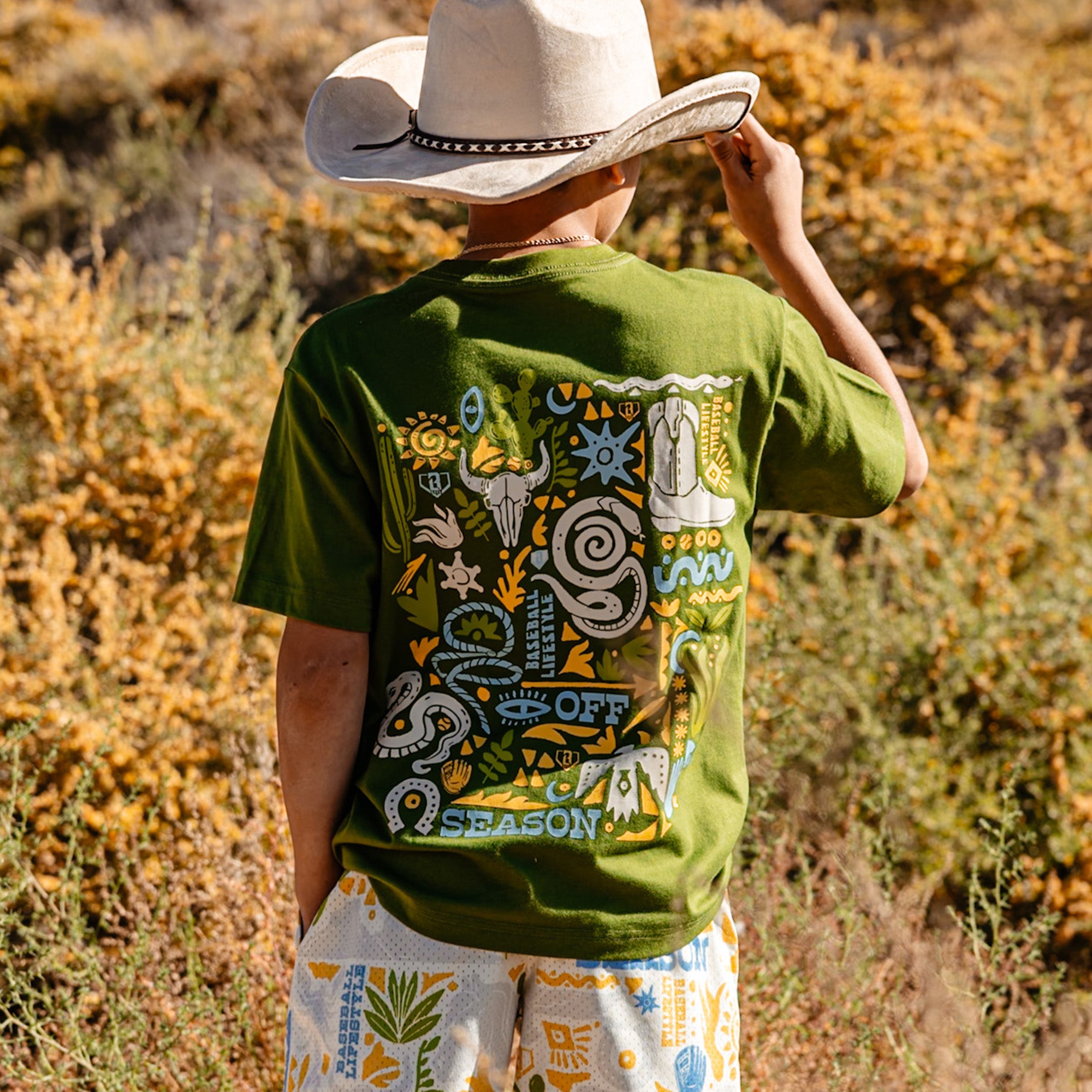Person wearing a green t-shirt with a colorful desert design, standing in a natural setting.