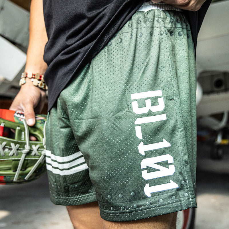Close up of Green athletic shorts with white waistband, BL101 logo on side, and star logo with stripes on bottom.